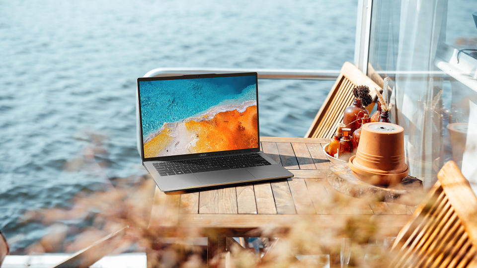 Lifestyle marketing image of Acer Swift Go 14 on an outdoor table by the beach.